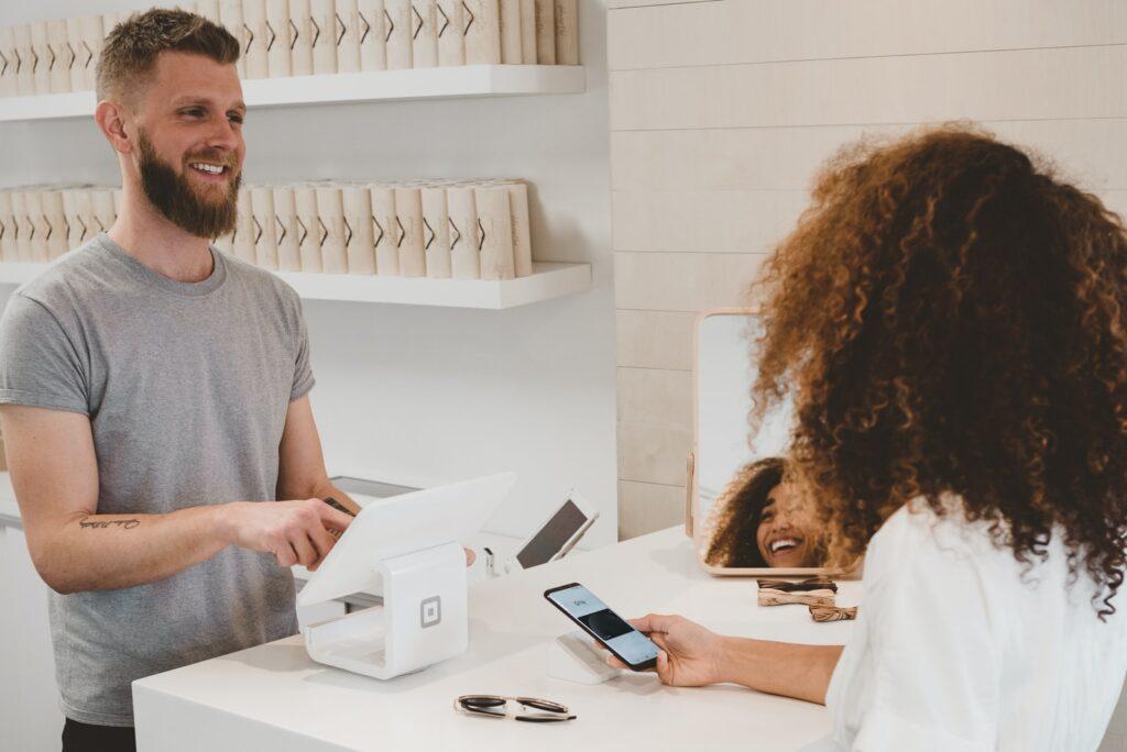 customer reviews request man in grey crew-neck t-shirt smiling to woman on counter